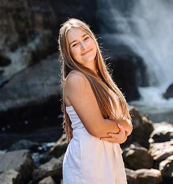 Mercedes Bales crosses her arms in front of a waterfall while posing for a photo.