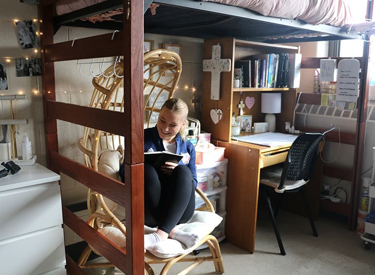 student in dorm room on bed